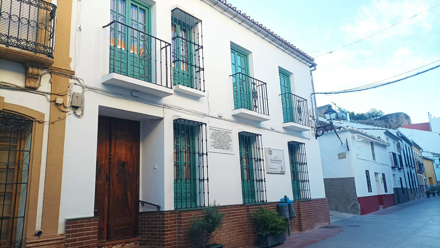Fachada encalada de la casa sede en El Burgo, con balcones de rejería y carpintería verde